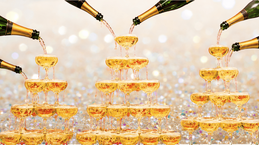Cascading champagne tower of glasses, with bottles of champagne pouring wine, overflowing the piles of glasses.